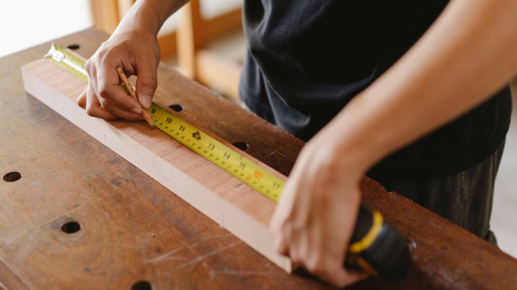 moderne Website für Handwerker: Handwerker an Werkbank misst Werkstück aus Holz mit Maßband aus